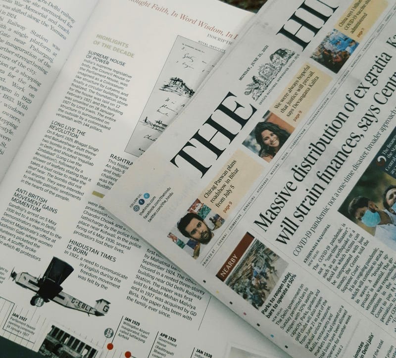 A folded newspaper lies across another paper’s open feature page, their headlines, columns and photographs in view.