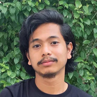 Redza Remee, writer at Carraway & Willow, with dark wavy hair and a goatee, in a black t-shirt before green leaves.
